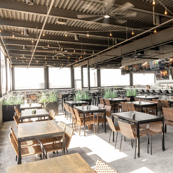 Spacious Black Hawk Brewery sports bar patio with tables, chairs, and a long bar with TVs.