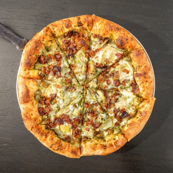 Overhead view of a Black Hawk Brewery pizza with pesto, artichokes, bacon, and cheese.