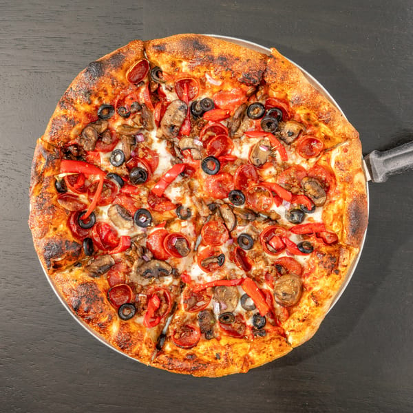 Overhead view of a Black Hawk Brewery pizza with pepperoni, olives, mushrooms, and red peppers.