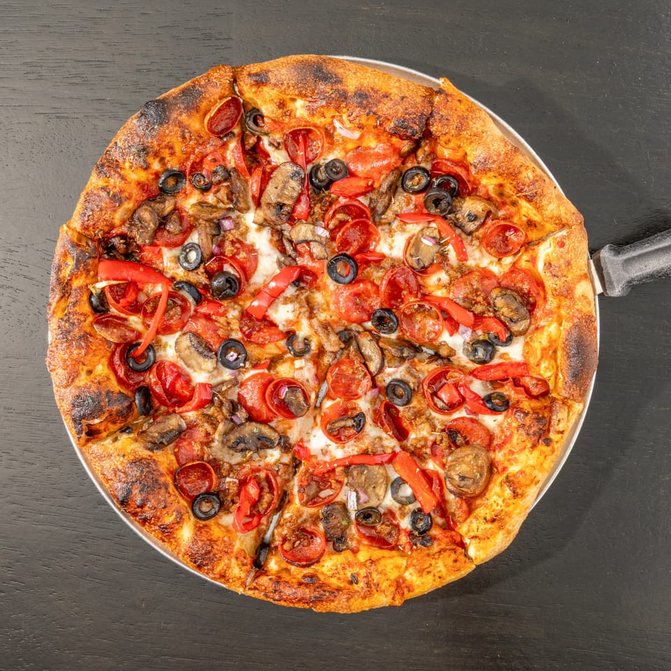 Overhead view of a Black Hawk Brewery pizza with pepperoni, olives, mushrooms, and red peppers.