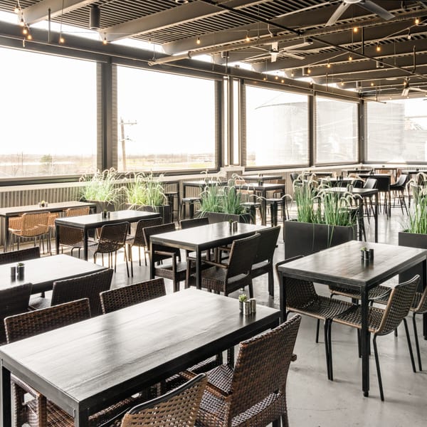 Black Hawk Brewery's spacious outdoor patio with dark tables, wicker chairs, and tall green plants.