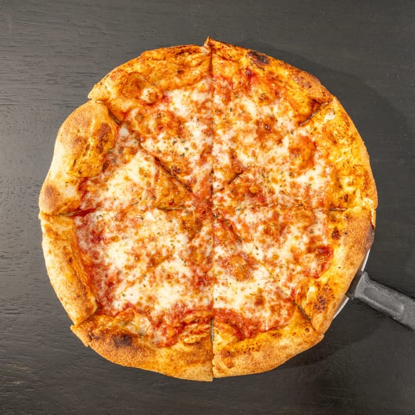 A Black Hawk Brewery cheese pizza, cut into slices, on a dark surface with a pizza server.